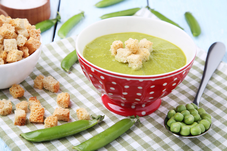 Green peas soup in bowl with rusks on wooden tableの写真素材