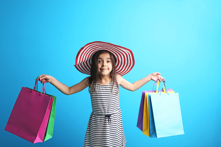 Beautiful little girl with hat and shopping bags on blue backgroundの写真素材