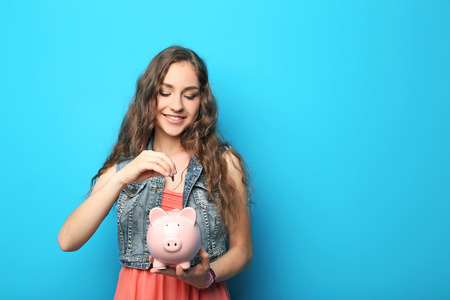 Portrait of young woman with piggy bank on blue backgroundの写真素材