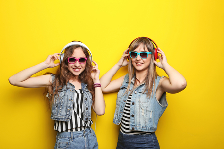 Portrait of two young woman with sunglasses and headphones on yellow backgroundの写真素材