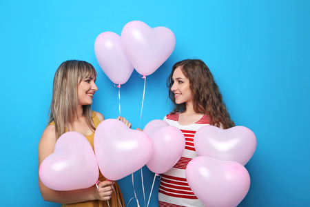 Two young woman with pink heart balloons on blue backgroundの写真素材
