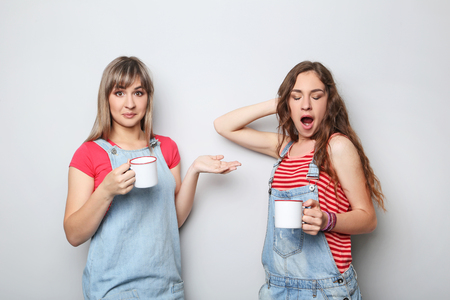 Portrait of two young woman with cups of coffee on grey backgroundの写真素材