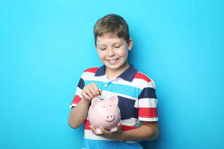 Portrait of young boy with piggy bank on blue backgroundの写真素材
