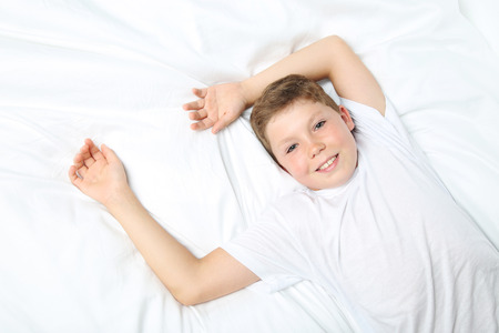 Young boy sleeping in white bedの写真素材