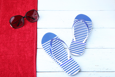 Pair of flip flops with towel and sunglasses on wooden tableの写真素材