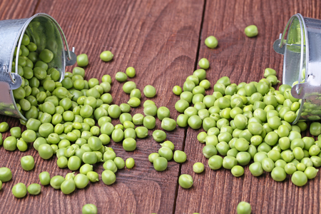 Fresh green peas in bucket on brown wooden tableの写真素材