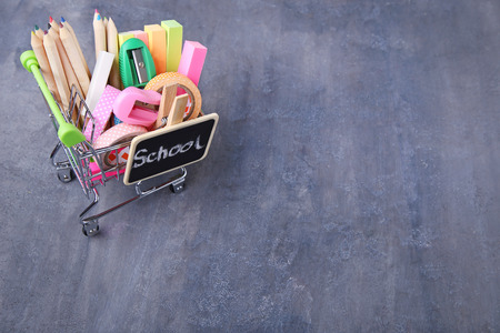 Shopping cart with school supplies on grey wooden tableの写真素材