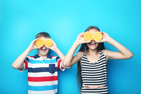 Young boy and girl with orange fruit on blue backgroundの写真素材