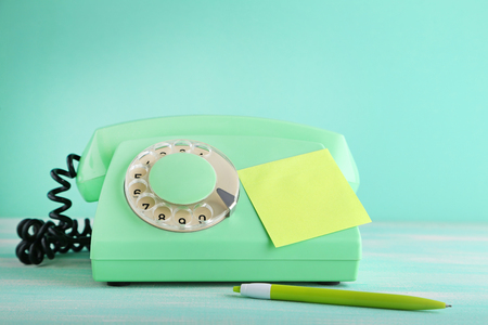 Green retro telephone with sticky note and pen on wooden tableの写真素材