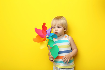 Portrait of little boy with rainbow whirligig on yellow backgroundの写真素材