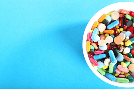 Different colorful pills in bowl on blue backgroundの写真素材