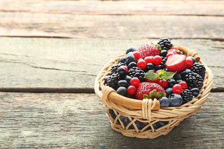 Ripe and sweet berries in basket on wooden tableの写真素材