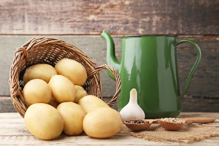 Potatoes in wicker basket with pepper and garlic on wooden backgroundの写真素材