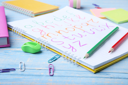 Handwritten alphabet in notebook with stationery on blue wooden tableの写真素材
