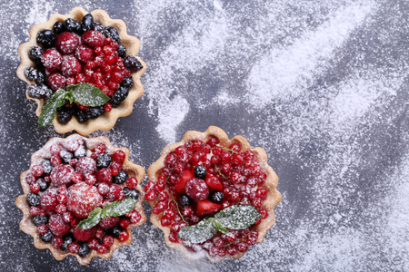 Dessert tartlets with berries and powdered sugar on grey wooden tableの写真素材