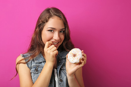 Portrait of young woman with sweet donut on pink backgroundの写真素材