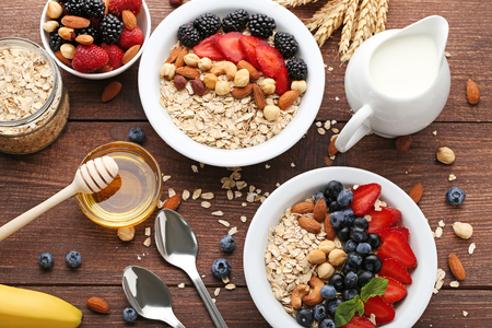 Oat flakes in plate with berries, nuts, honey and milk on wooden tableの写真素材