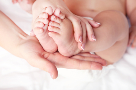 Newborn baby feet in mother hands on white bedの写真素材