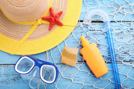 Sunscreen with diving mask, snorkel and hat on wooden table