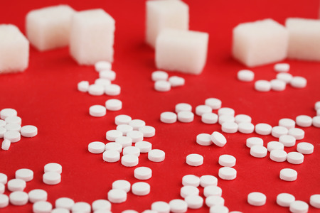 Sweetener tablets and sugar cubes on red backgroundの写真素材