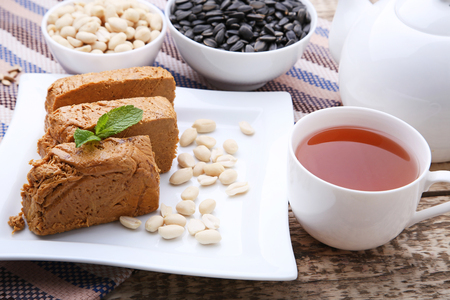 Tasty slices of halva in white plate with cup of tea on wooden tableの写真素材