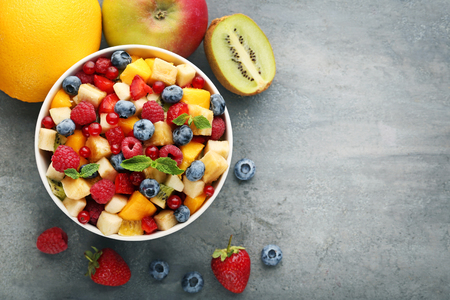 Fresh fruit salad in bowl on grey wooden tableの写真素材