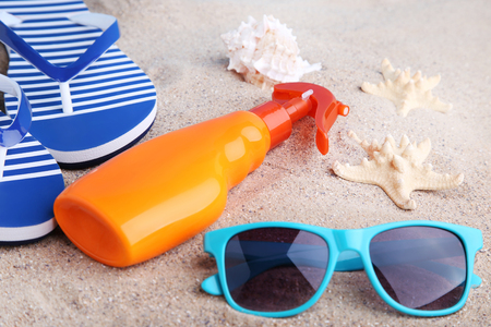 Sunscreen with flip flop and sunglasses on beach sandの写真素材