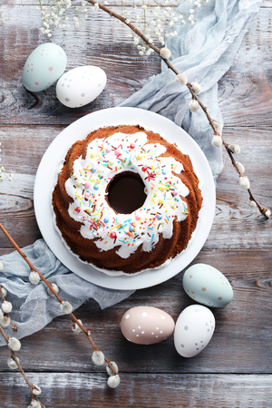 Bundt cake with sprinkles and easter eggs on wooden table