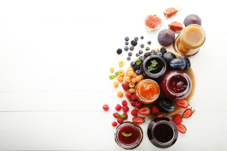 Glass jars with different kinds of jam and berries on wooden table