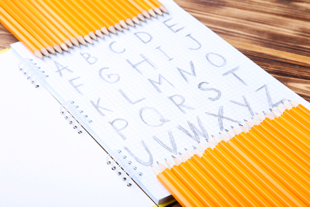 Handwritten alphabet in notebook with pencils on brown wooden tableの写真素材