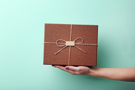 Female hand holding gift box on mint backgroundの写真素材