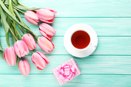 Pink tulips with gift box and cup of tea on wooden tableの写真素材