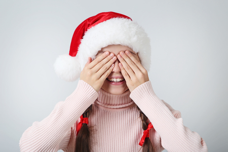 Young girl in santa hat with closed eyes by hands on grey backgroundの写真素材