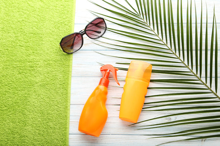 Sunscreen with towel and sunglasses on white wooden table