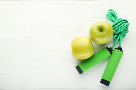 Green skipping rope with apple on white wooden tableの写真素材