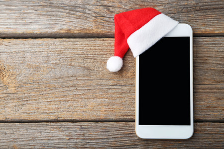 Smartphone with red santa hat on grey wooden tableの写真素材