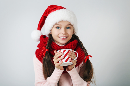 Young girl in santa hat with scarf and cup of tea on grey backgroundの写真素材