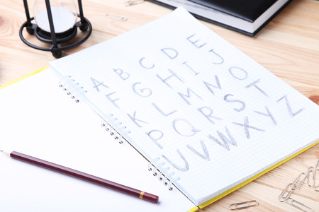 Handwritten alphabet in notebook with pencils on brown wooden table
