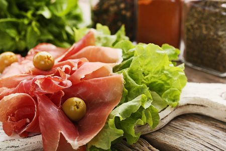 Slices of jamon with olives and lettuce on white cutting boardの写真素材