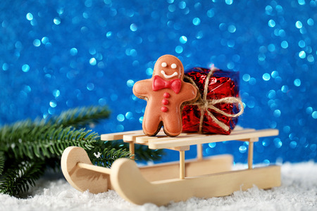 Wooden toy sleigh with gingerbread cookie and gift box on lights background
