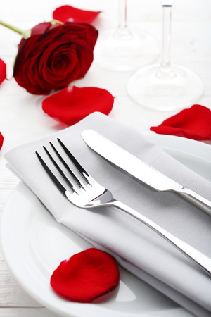 Kitchen cutlery in white plate with red rose petals on wooden tableの写真素材
