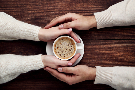 Female and male hand holding cup of coffee on wooden tableの写真素材