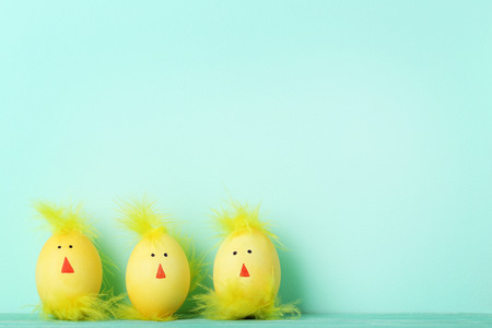Yellow eggs with funny chicken faces on mint background