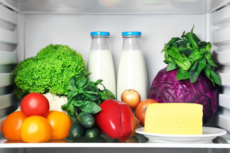 Open fridge full of vegetables with cheese and bottle of milkの写真素材