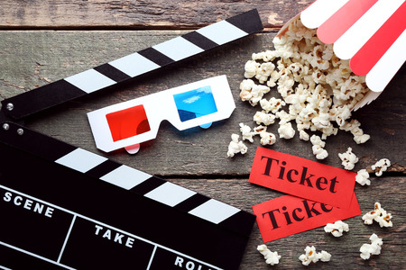 Clapper board with popcorn in striped bucket and glasses on wooden table