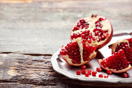 Ripe and juicy pomegranate in tray on grey wooden tableの写真素材