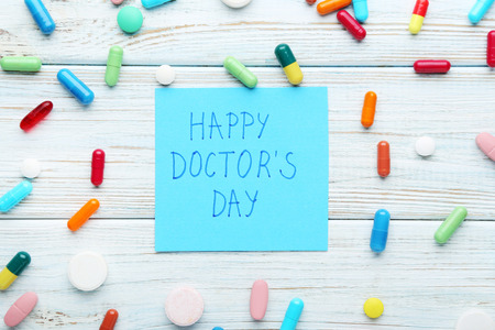 Inscription Happy Doctors Day with pills and capsule on wooden tableの写真素材