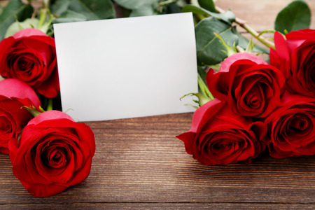 Bouquet of red roses with sheet of blank paper on brown wooden tableの写真素材