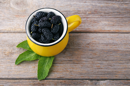 Black mulberries in mug on wooden tableの写真素材