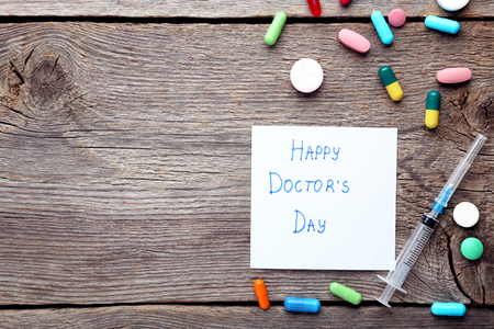Inscription Happy Doctors Day with pills and syringe on wooden tableの写真素材